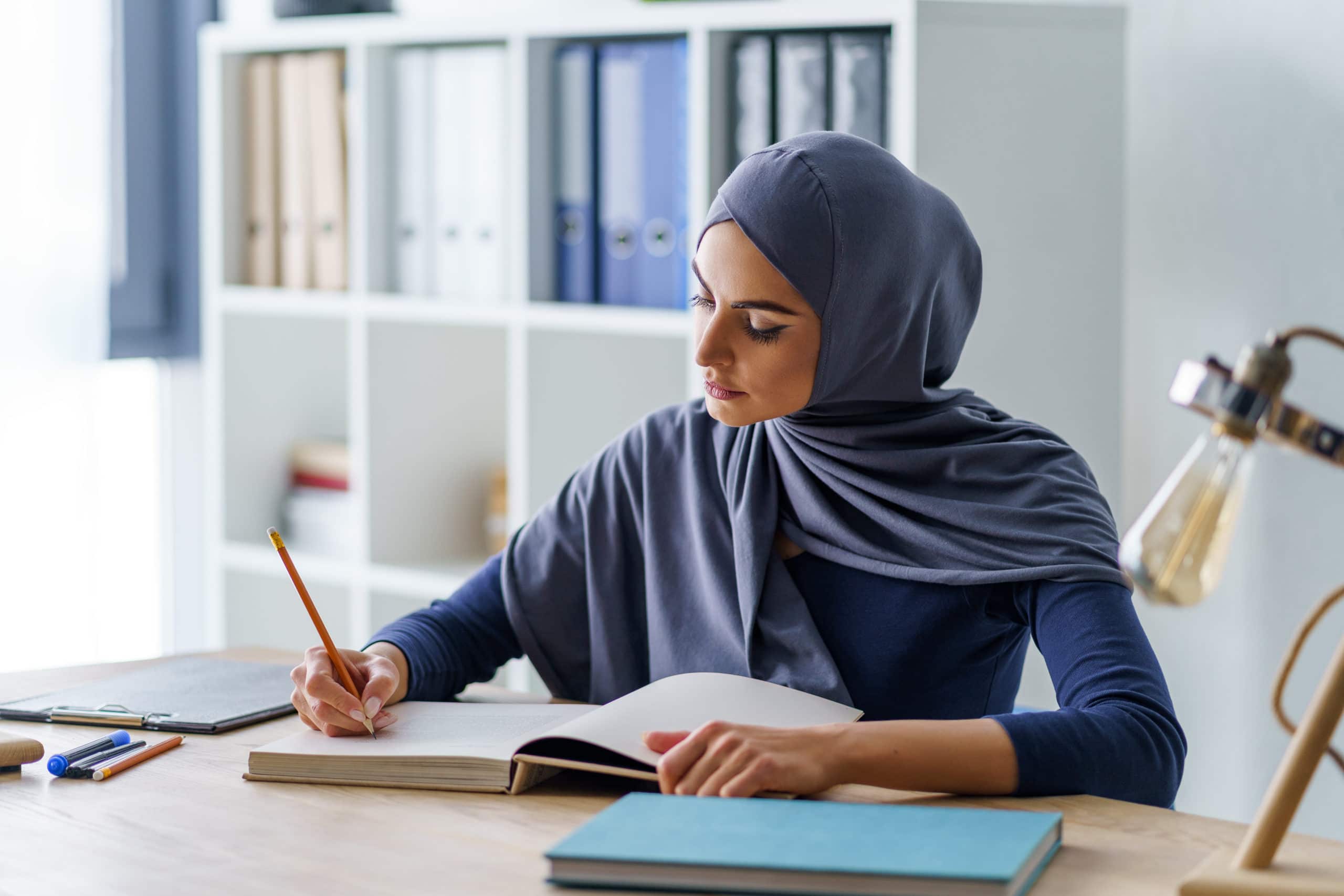 Female Muslim professor taking a note in a book, getting ready for classes. Woman fully absorbed in work.