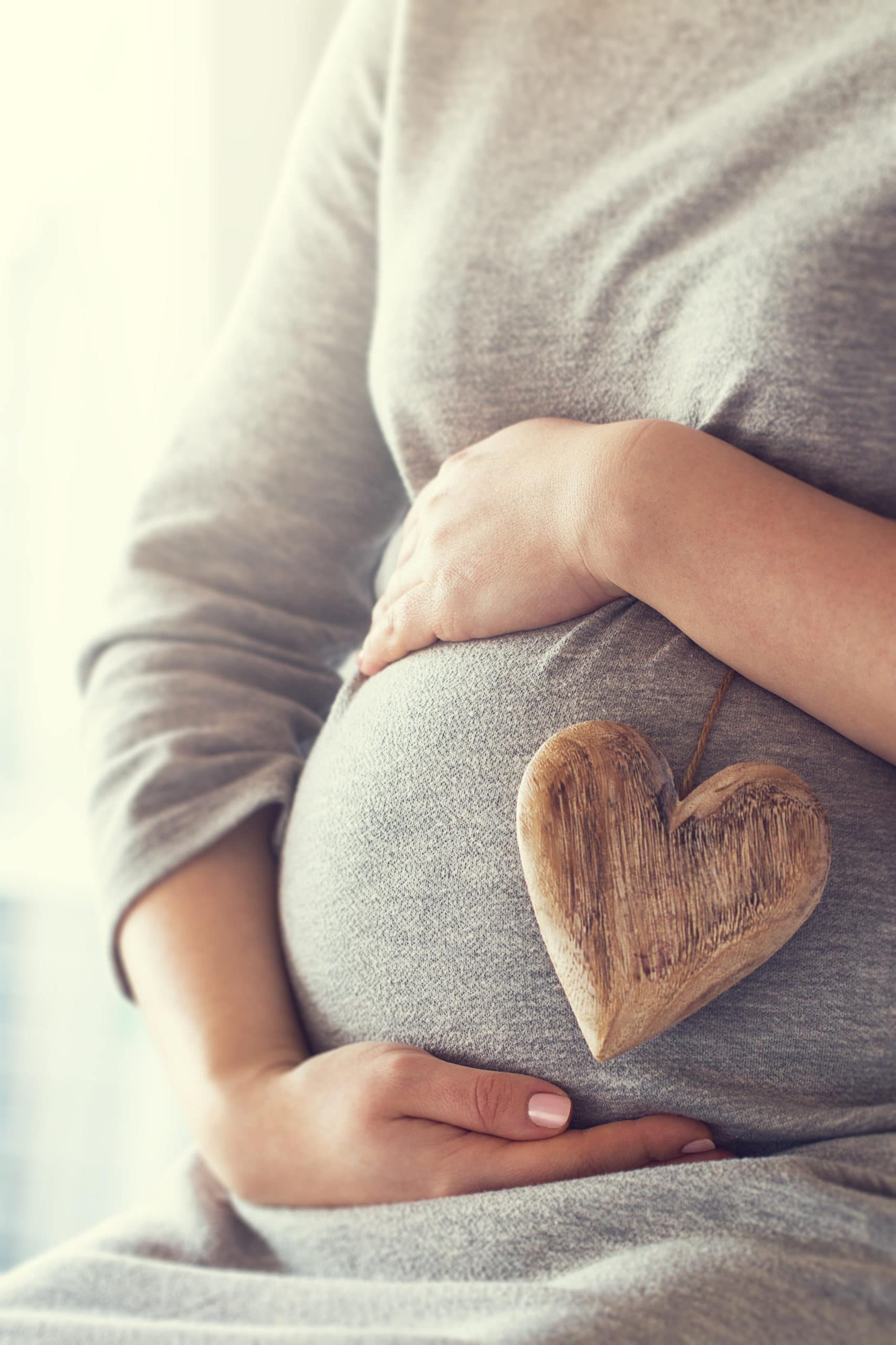 Young pregnant woman holds wooden heart. Love concept. Pastel toning