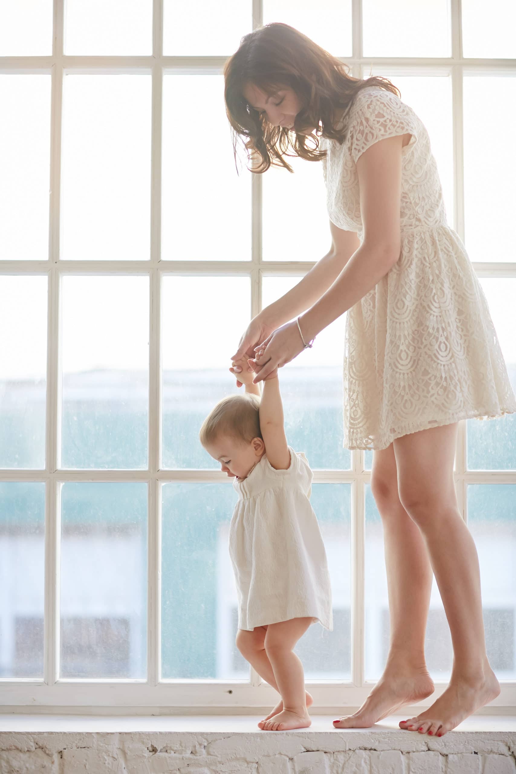 Baby taking first steps with mother's help at home. Baby leaning walking with mother