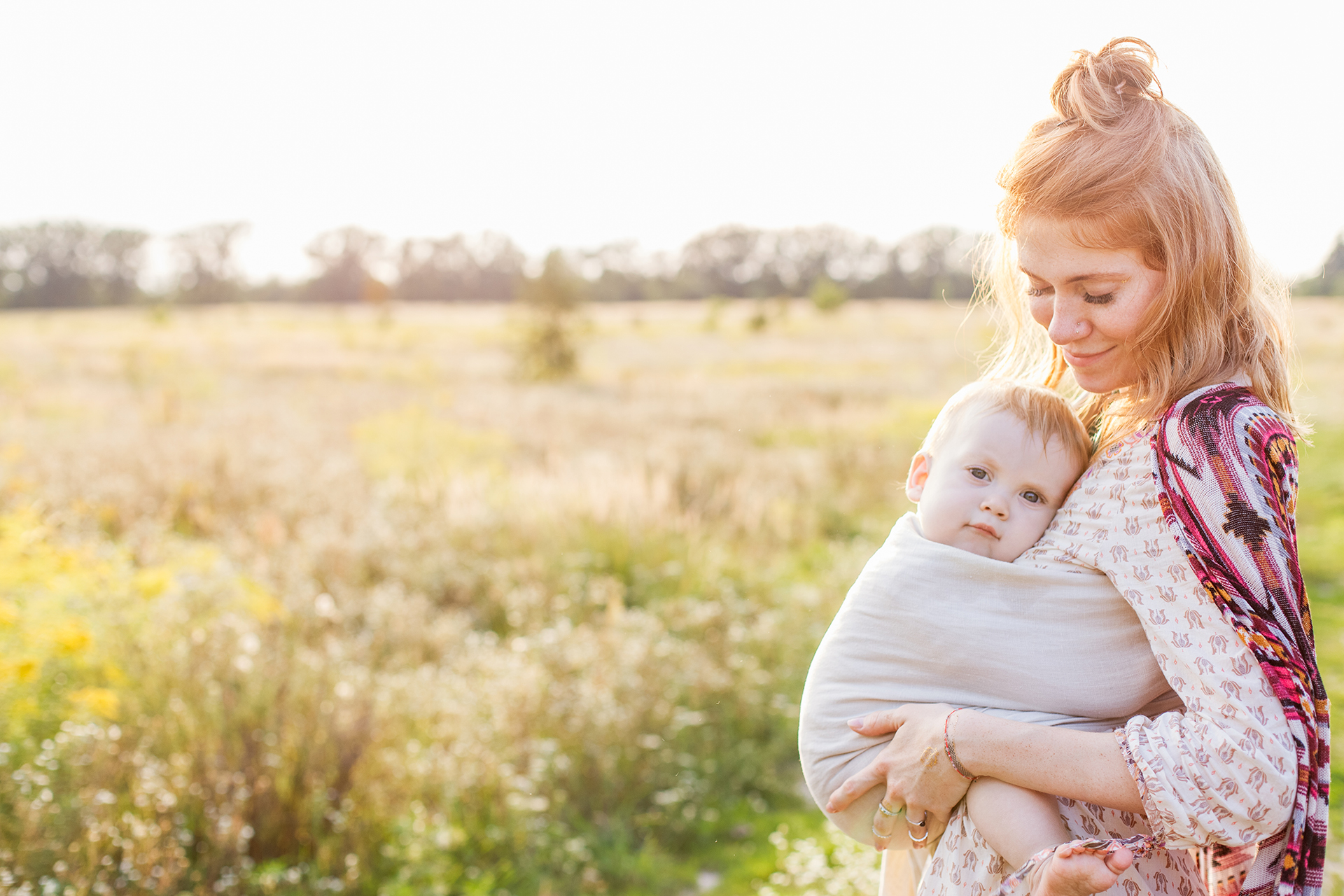 Little,Baby,Boy,And,His,Mother,Walking,In,The,Fields. Little baby boy and his mother walking in the fields. Mother is holding and tickling her baby, babywearing in sling