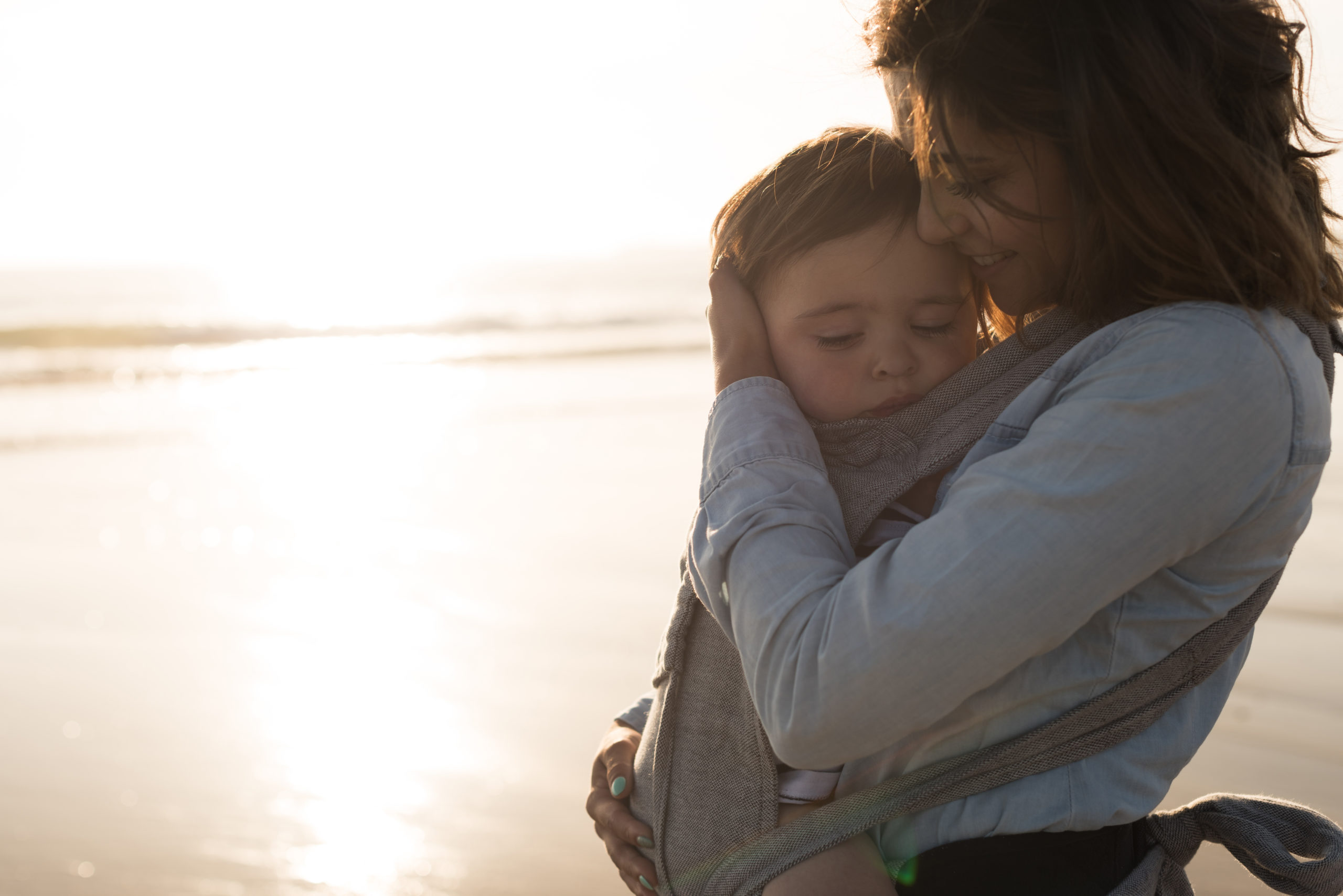 Mother,With,Ergobaby,Carrying,Toddler,On,The,Beach