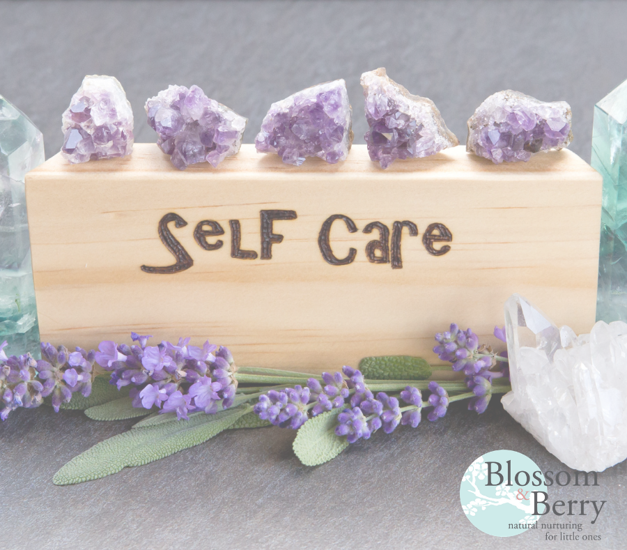 Picture of a piece of wood with the word self care on surrounded by crystals and flowers