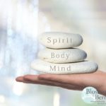 Picture of a hand holding 3 stones with the words spirit body and mind on each