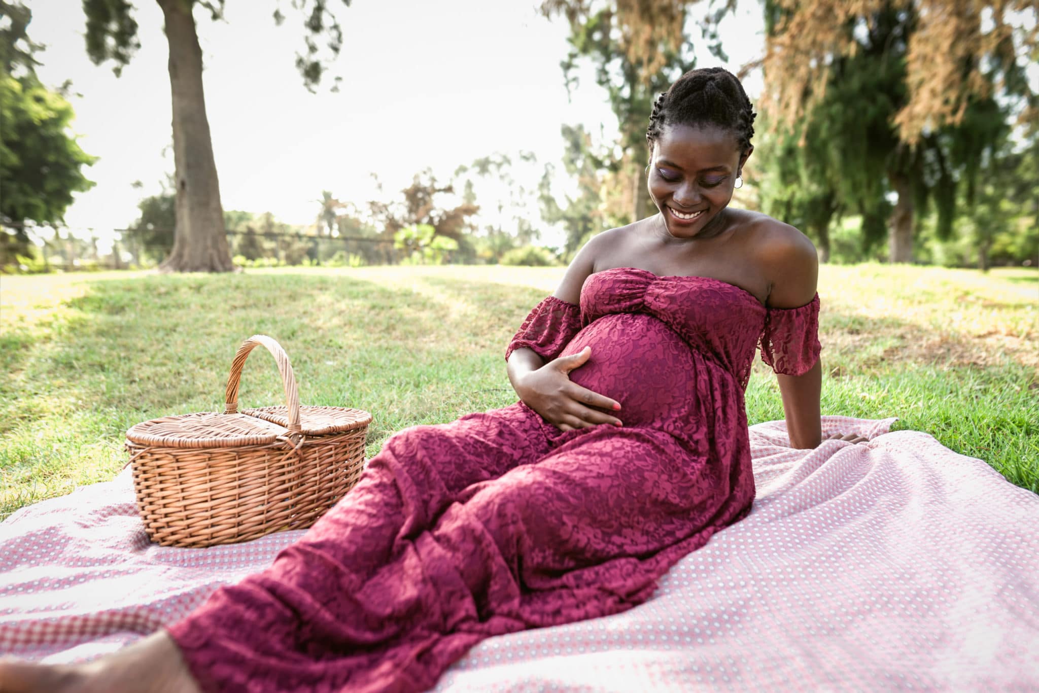 African,Woman,Caressing,Her,Pregnant,Belly,While,Doing,A,Picnic