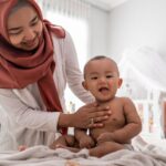 The History of Baby Massage in the Middle East - picture of a lady in a headscarf massing a baby on a bed