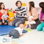 How to Become a Baby Yoga Instructor – Training, Certification & Career Guide - picture of a group of parents and babies with a yoga mat on the floor and a toddler on the floor crawling